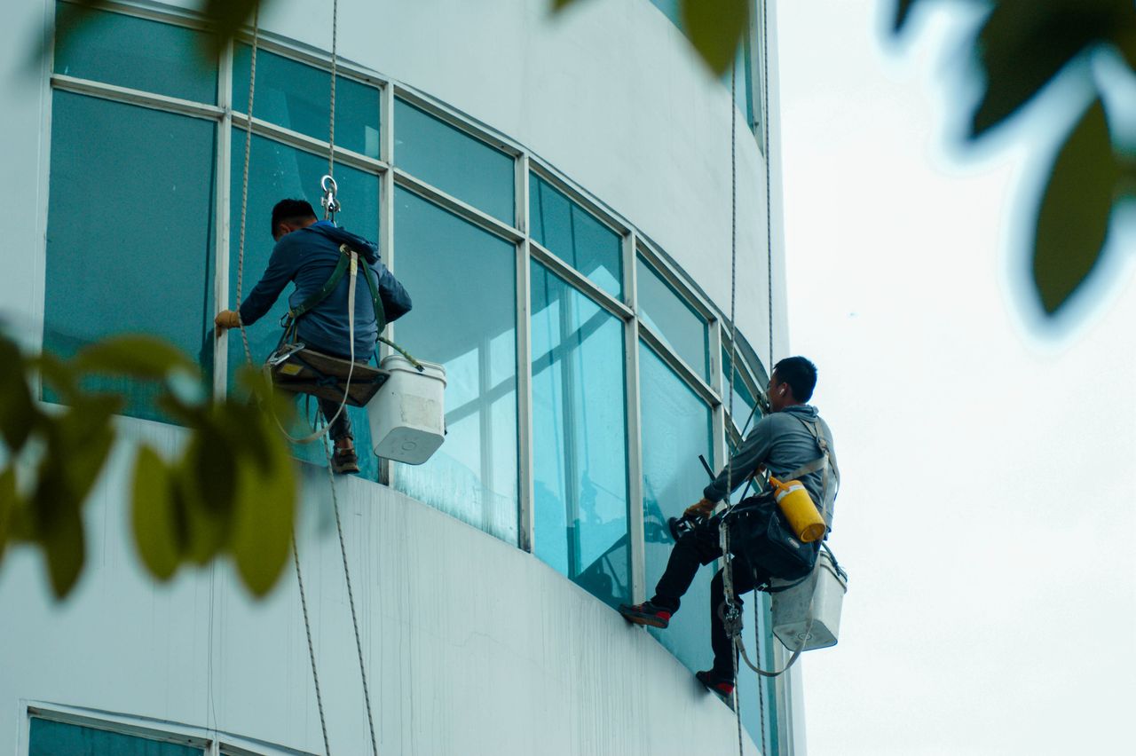 Des laveurs de vitres suspendus à des cordes nettoient la façade vitrée d’immeubles de grande hauteur.