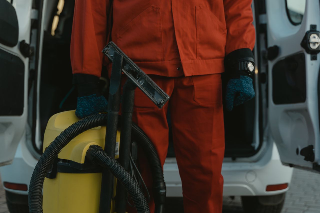 Un professionnel du nettoyage en uniforme rouge, tenant un aspirateur près d’un van, prêt à intervenir.